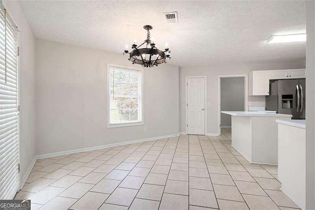 unfurnished dining area with a chandelier, a textured ceiling, light tile patterned floors, and baseboards