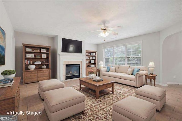 living area featuring ceiling fan, a tile fireplace, baseboards, and arched walkways