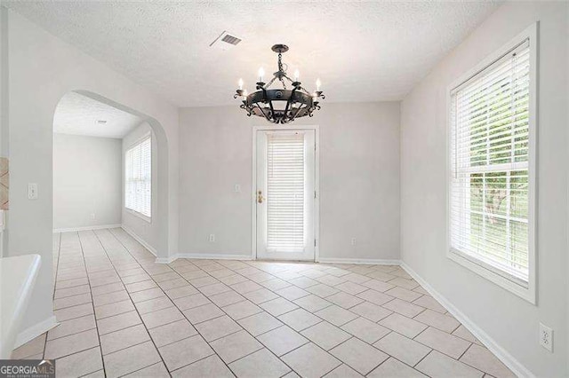 unfurnished room featuring a chandelier, arched walkways, light tile patterned floors, a textured ceiling, and baseboards