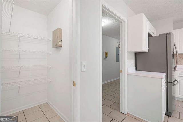 corridor with a textured ceiling, light tile patterned flooring, baseboards, and electric panel