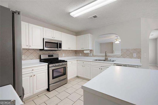 kitchen featuring stainless steel appliances, a sink, arched walkways, a textured ceiling, and white cabinetry