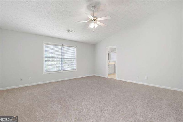 empty room featuring a textured ceiling, a ceiling fan, light carpet, baseboards, and vaulted ceiling