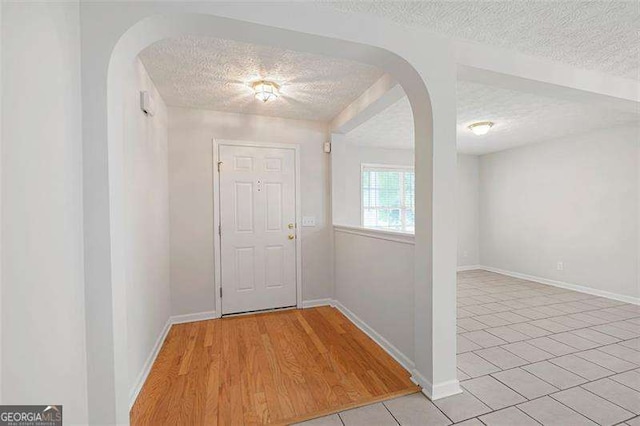 entrance foyer featuring a textured ceiling, arched walkways, light tile patterned floors, and baseboards