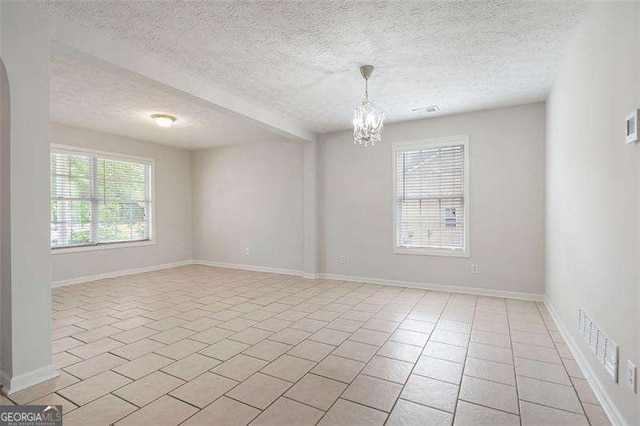 spare room featuring healthy amount of natural light, a chandelier, a textured ceiling, baseboards, and light tile patterned floors