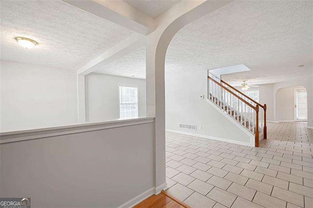 corridor with arched walkways, a textured ceiling, stairway, baseboards, and tile patterned floors