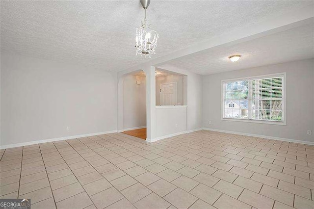 empty room featuring a textured ceiling, arched walkways, a chandelier, and baseboards