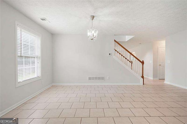 empty room featuring stairway, a chandelier, healthy amount of natural light, a textured ceiling, and baseboards