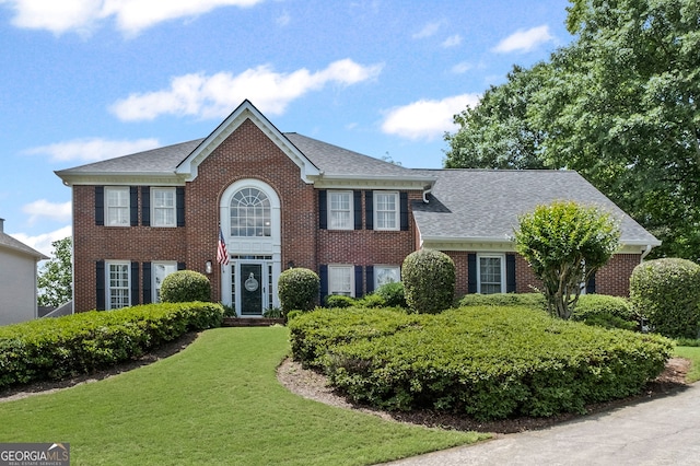 colonial house featuring a front lawn, brick siding, and roof with shingles