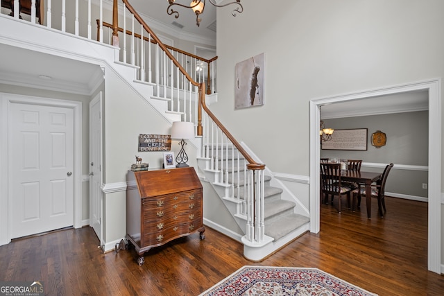 staircase featuring a chandelier, wood finished floors, crown molding, a towering ceiling, and baseboards