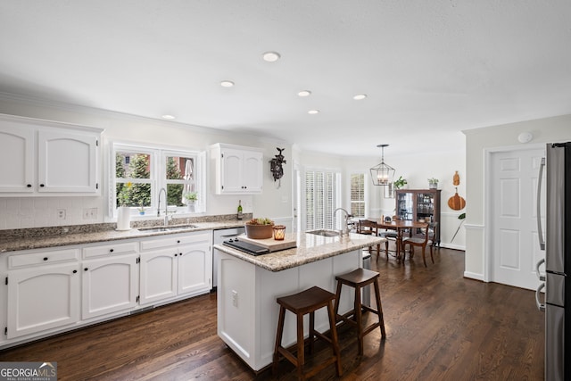 kitchen with a sink, freestanding refrigerator, white cabinets, a kitchen breakfast bar, and dark wood finished floors
