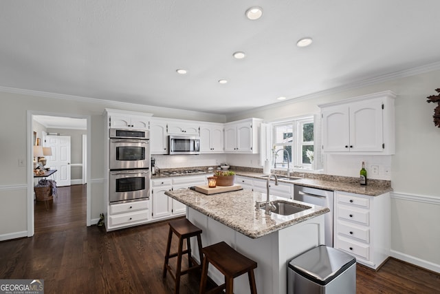kitchen featuring appliances with stainless steel finishes, a sink, white cabinetry, ornamental molding, and a center island with sink