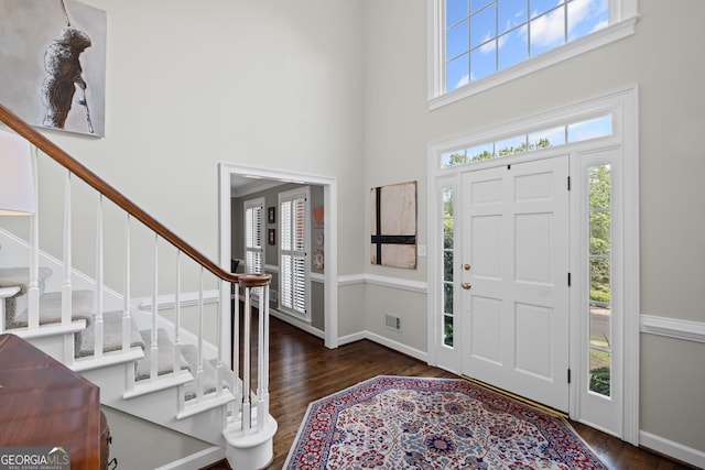 foyer entrance with a towering ceiling, dark wood-style floors, stairs, and baseboards
