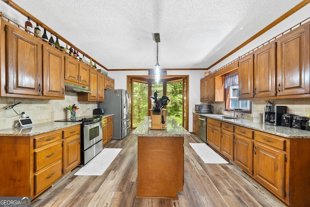 kitchen featuring appliances with stainless steel finishes, a kitchen island, crown molding, under cabinet range hood, and tasteful backsplash