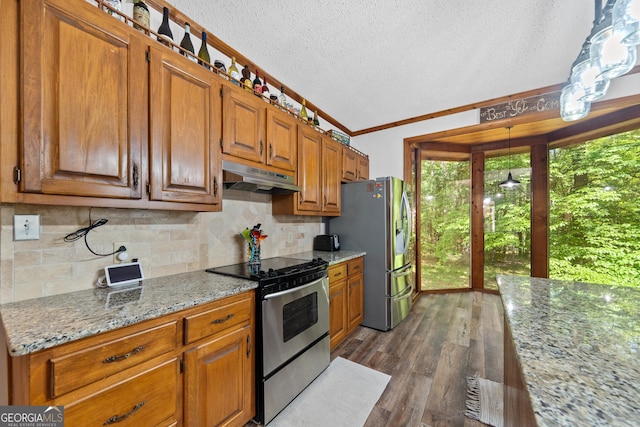 kitchen with under cabinet range hood, appliances with stainless steel finishes, a textured ceiling, brown cabinets, and crown molding