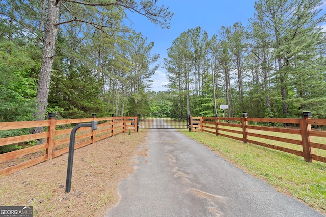 view of asphalt driveway with a gate and a forest view