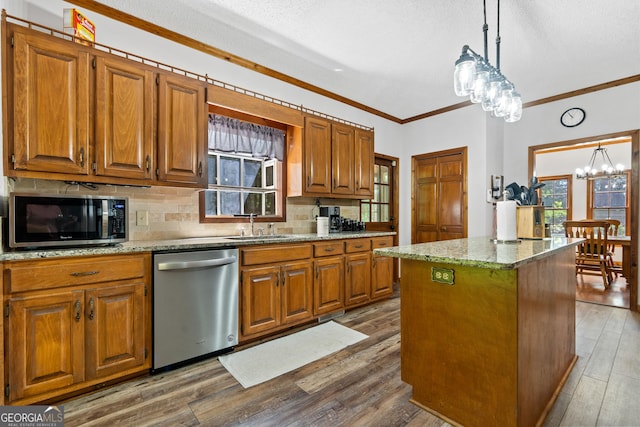 kitchen with appliances with stainless steel finishes, a chandelier, plenty of natural light, crown molding, and backsplash