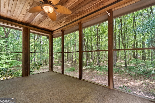 unfurnished sunroom with ceiling fan and a forest view