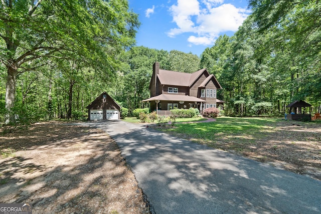 view of front of home featuring an outdoor structure, a detached garage, a chimney, and a view of trees
