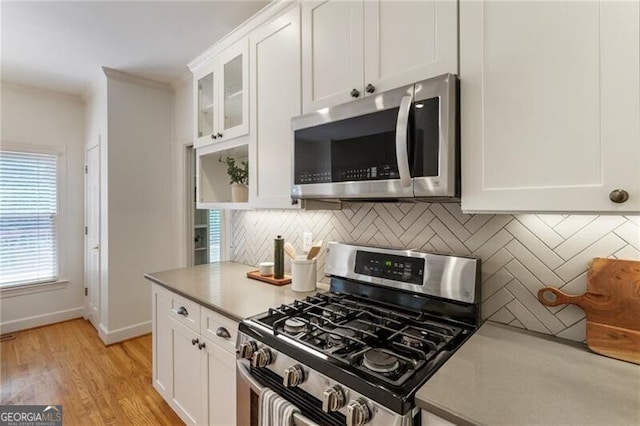 kitchen with appliances with stainless steel finishes, backsplash, white cabinetry, glass insert cabinets, and light wood-style floors