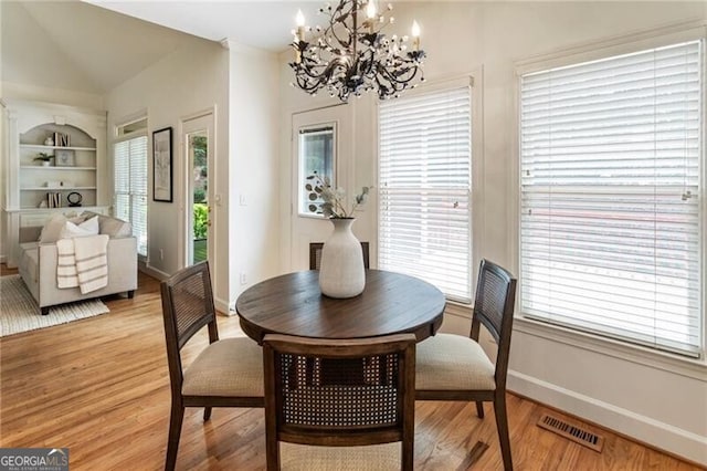 dining room featuring a chandelier, light wood-type flooring, plenty of natural light, baseboards, and vaulted ceiling