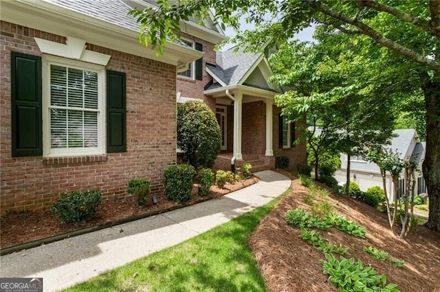 view of exterior entry with brick siding and a shingled roof