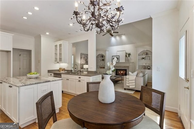dining space featuring a lit fireplace, crown molding, recessed lighting, built in features, and light wood-style flooring