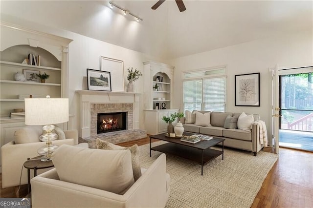 living area featuring rail lighting, built in shelves, wood finished floors, ceiling fan, and lofted ceiling