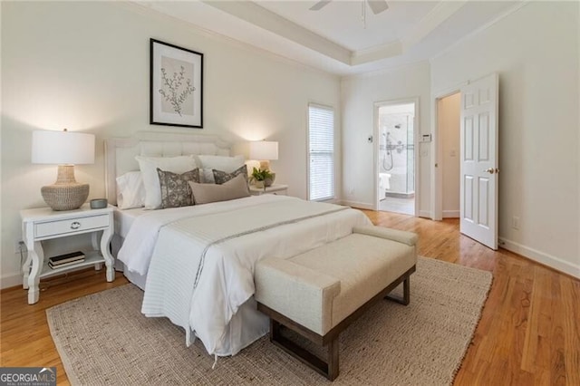 bedroom with a raised ceiling, light wood-type flooring, baseboards, connected bathroom, and a ceiling fan