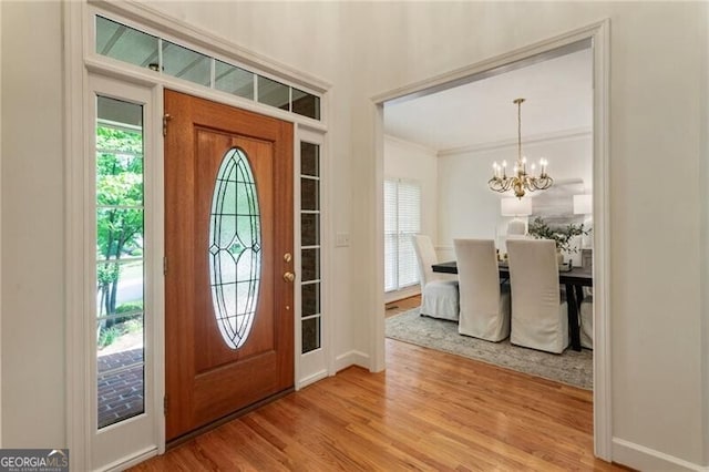 entryway featuring plenty of natural light, wood finished floors, a chandelier, ornamental molding, and baseboards