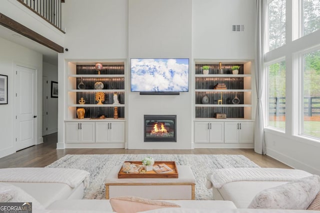 living area featuring a towering ceiling, built in features, wood finished floors, a glass covered fireplace, and baseboards