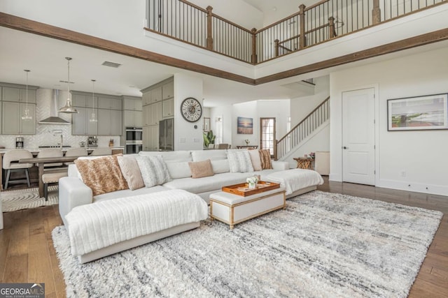 living room with a towering ceiling, stairway, and dark wood-style floors