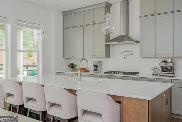 kitchen with wall chimney range hood, gas stovetop, gray cabinetry, and light countertops