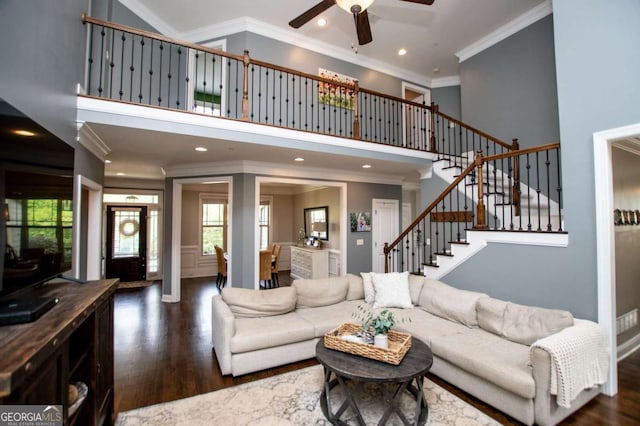 living area with crown molding, wood finished floors, a ceiling fan, stairway, and a high ceiling