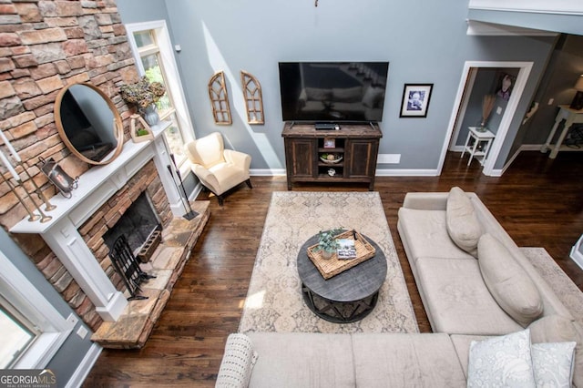 living room featuring a stone fireplace, baseboards, and dark wood finished floors