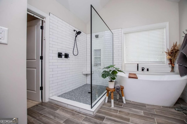 bathroom with tiled shower, wood finish floors, a freestanding bath, and lofted ceiling