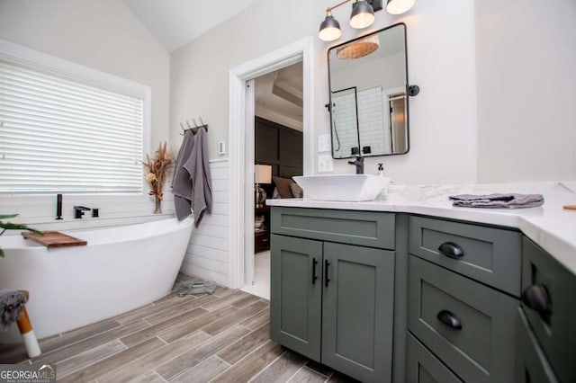 bathroom featuring wood finished floors, vanity, a freestanding tub, and lofted ceiling