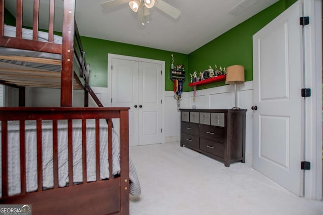 bedroom featuring carpet floors, a wainscoted wall, a ceiling fan, and a closet
