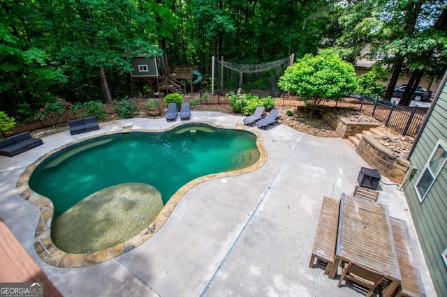 view of pool with a patio, fence, and view of wooded area