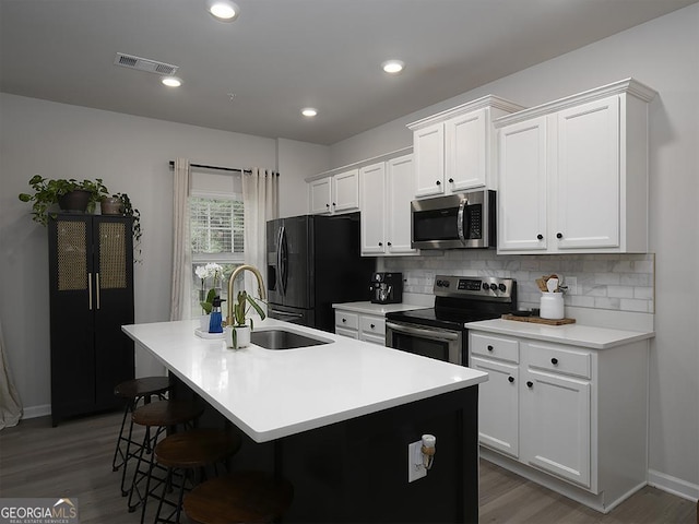 2108 Remy Ct, Kennesaw, GA 30144 - kitchen featuring appliances with stainless steel finishes, a sink, a kitchen island with sink, tasteful backsplash, and wood finished floors