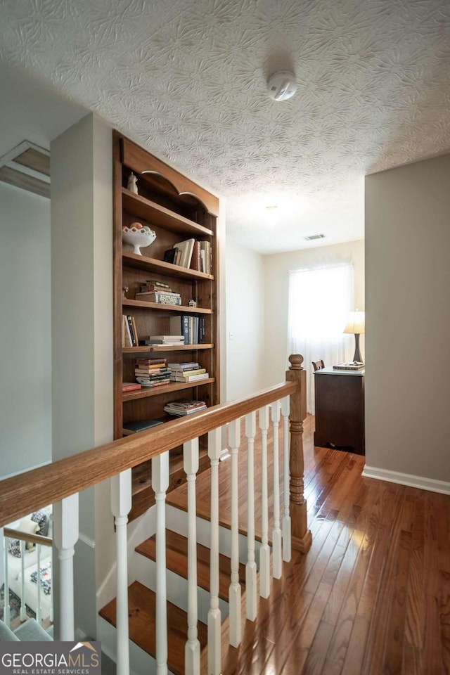 corridor with an upstairs landing, hardwood / wood-style flooring, baseboards, and a textured ceiling