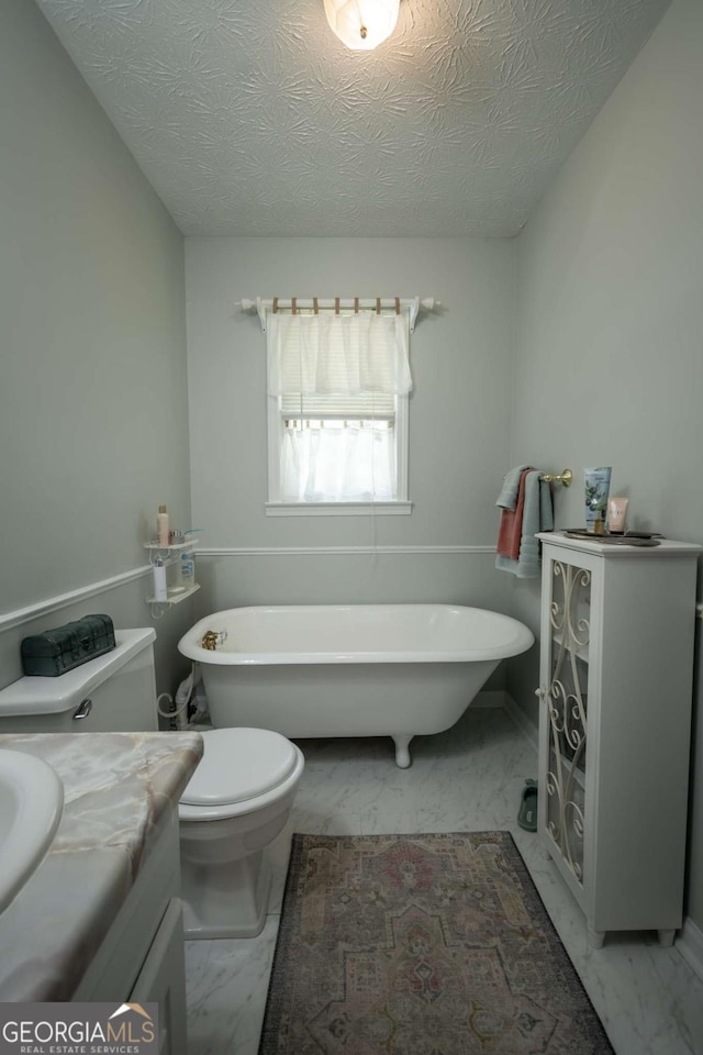 full bath with marble look tile flooring, a soaking tub, toilet, vanity, and a textured ceiling