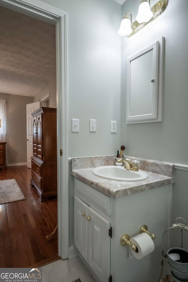 bathroom with vanity, a textured ceiling, baseboards, and wood finished floors
