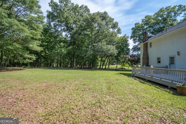 view of grassy yard featuring a wooden deck and view of wooded area