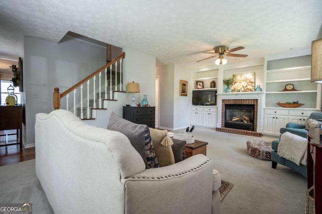 living room featuring a ceiling fan, baseboards, a brick fireplace, stairway, and a textured ceiling