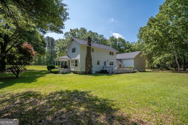 back of property with a chimney, a wooden deck, a yard, and view of wooded area