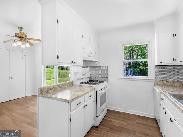 kitchen featuring white appliances, under cabinet range hood, tasteful backsplash, light countertops, and ornamental molding