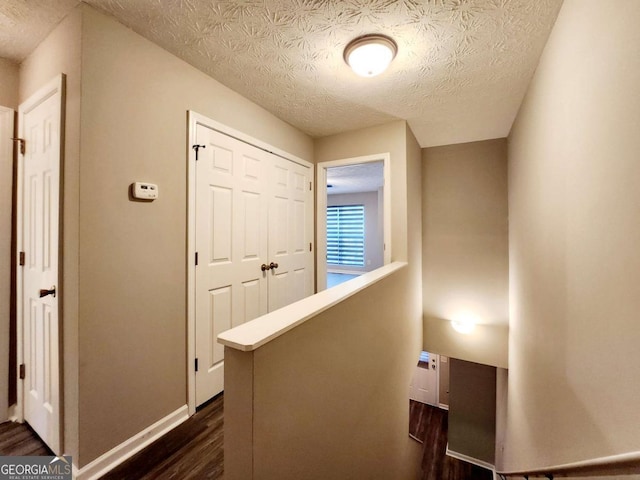 hallway with dark wood-style flooring, an upstairs landing, baseboards, and a textured ceiling
