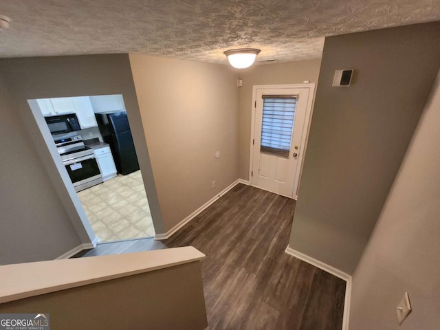 hall with baseboards, wood finished floors, and a textured ceiling