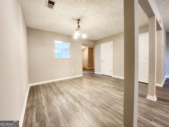 unfurnished dining area with wood finished floors, a textured ceiling, baseboards, and a chandelier