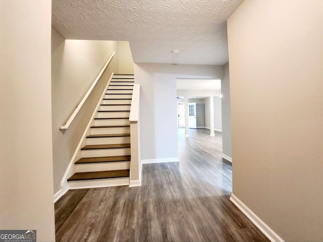 stairs with wood finished floors, baseboards, and a textured ceiling
